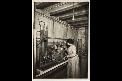 A black and white historical photo of a scientist working with some elaborate equipment in a lab
